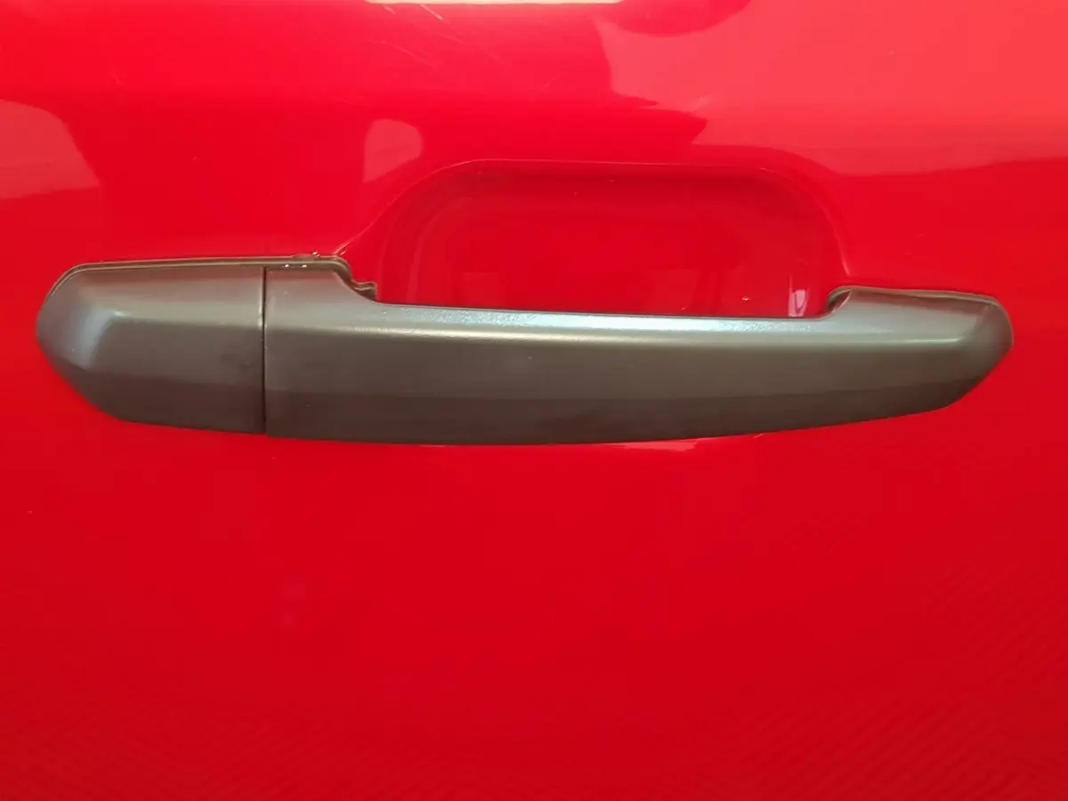 Poignée de porte grise sur la portière rouge d'une Aixam Ambition 0.5 City Pack 2026, vue en gros plan.