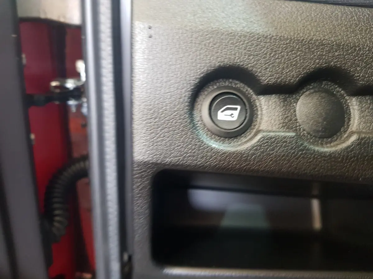 Bouton d'ouverture de coffre sur panneau intérieur noir d'une Aixam Ambition 0.5 City Pack rouge, vue rapprochée.