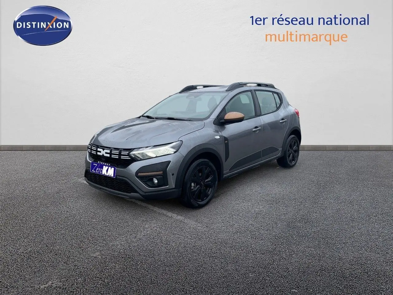 Vue 3/4 avant droite d'une Dacia Sandero Stepway 2024 gris schiste métal avec rétroviseurs bronze et jantes noires.