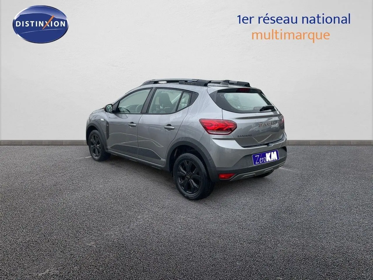 Vue 3/4 arrière droite d'une Dacia Sandero Stepway gris schiste métal avec jantes noires et barres de toit noires.