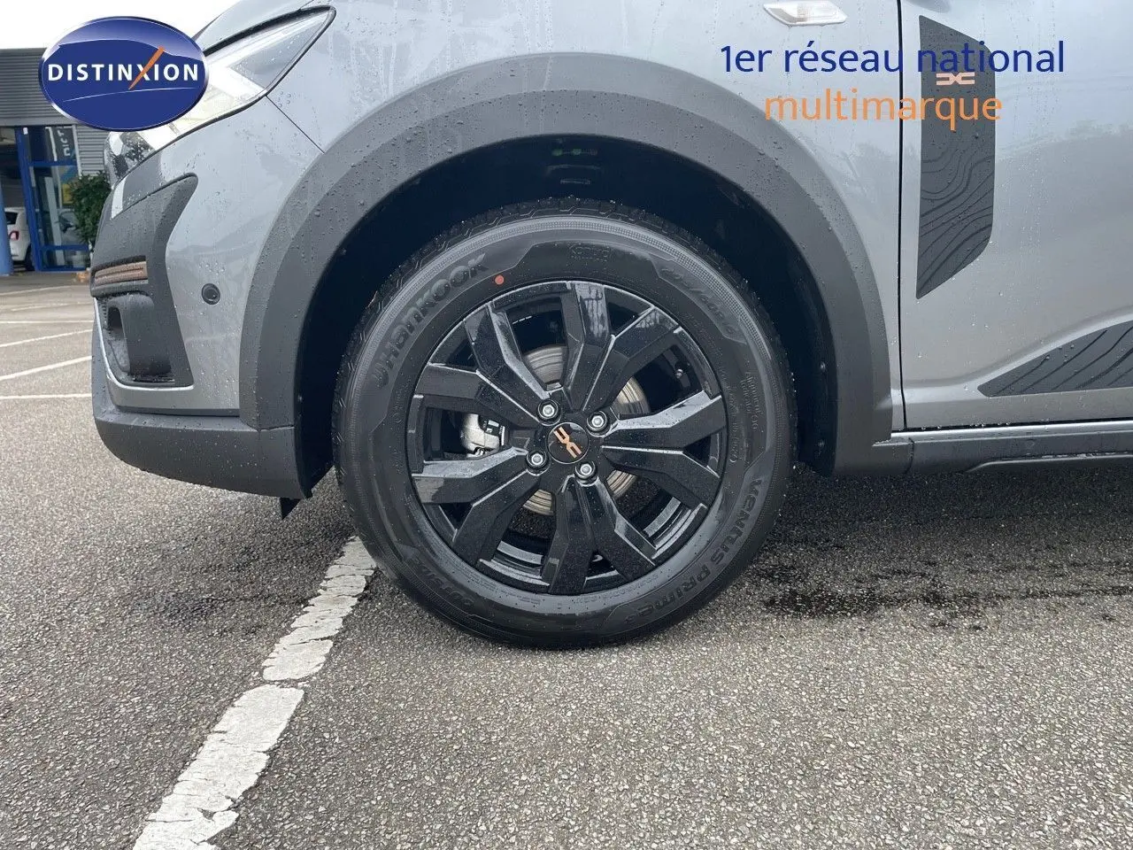 Gros plan sur la roue avant gauche noire et la partie basse grise schiste métallisée d'une Dacia Sandero Stepway 2024.