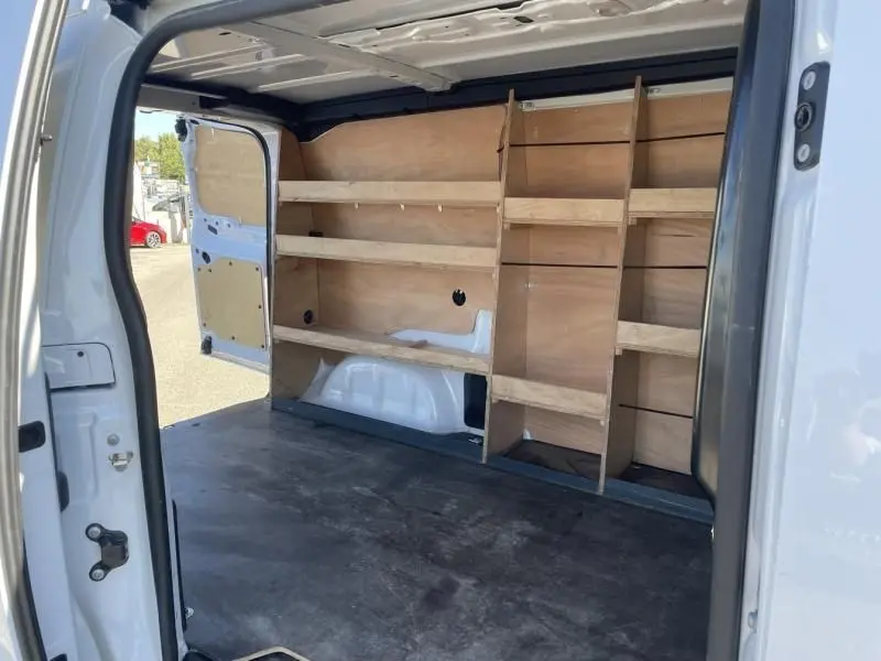 Intérieur du Peugeot Expert Fourgon blanc 2023 vu de l'arrière, montrant les étagères en bois installées côté gauche du coffre.