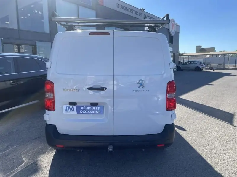 Vue arrière d'un Peugeot Expert Fourgon blanc 2023 avec porte-voiture sur le toit et plaque "Véhicules Occasions".