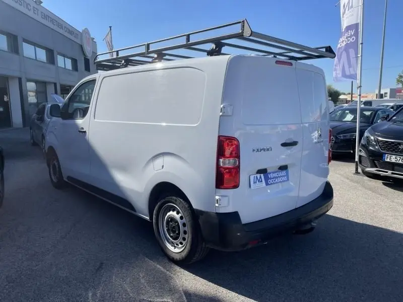 Vue 3/4 arrière droite d'un Peugeot Expert Fourgon blanc 2023 avec galerie de toit et porte latérale pleine.