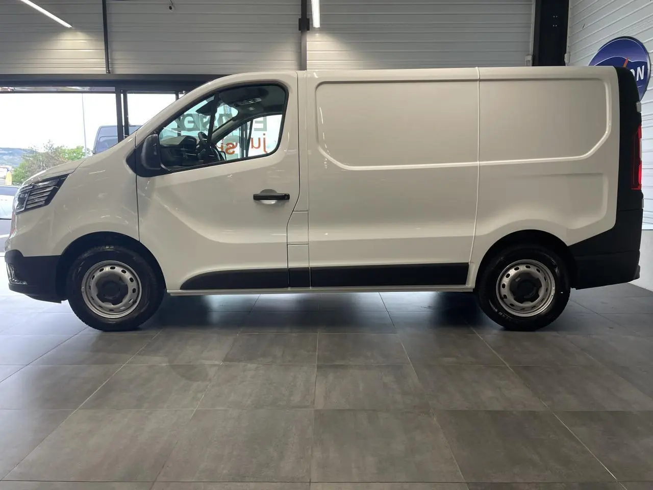 Profil droit du Renault Trafic Fourgon blanc 2025 avec jantes tôles et porte latérale coulissante visible en intérieur showroom.