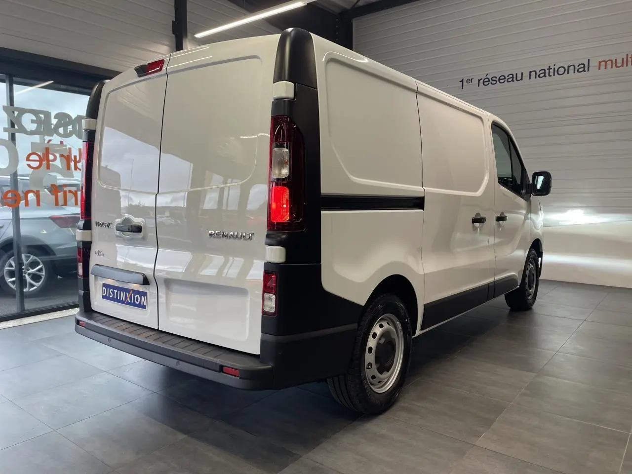 Renault Trafic Fourgon blanc en vue 3/4 arrière droit, avec feux arrière allumés et jantes tôles 16 pouces.