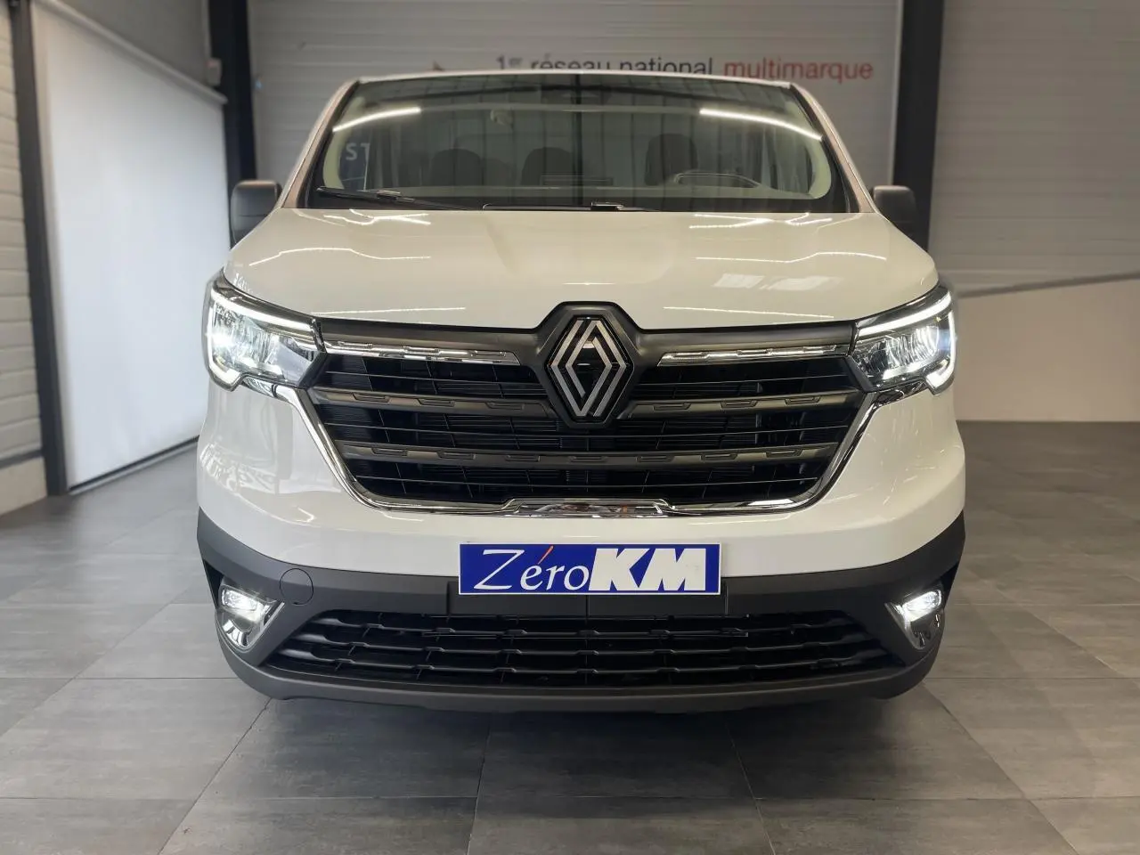 Vue frontale d'un Renault Trafic Fourgon blanc avec calandre noire et phares Full LED allumés en intérieur.