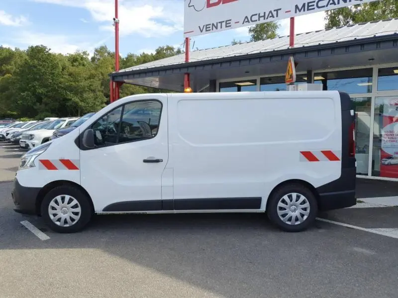 Profil côté gauche d'un utilitaire Renault Trafic blanc glacier avec bandes réfléchissantes rouges sur porte et arrière.