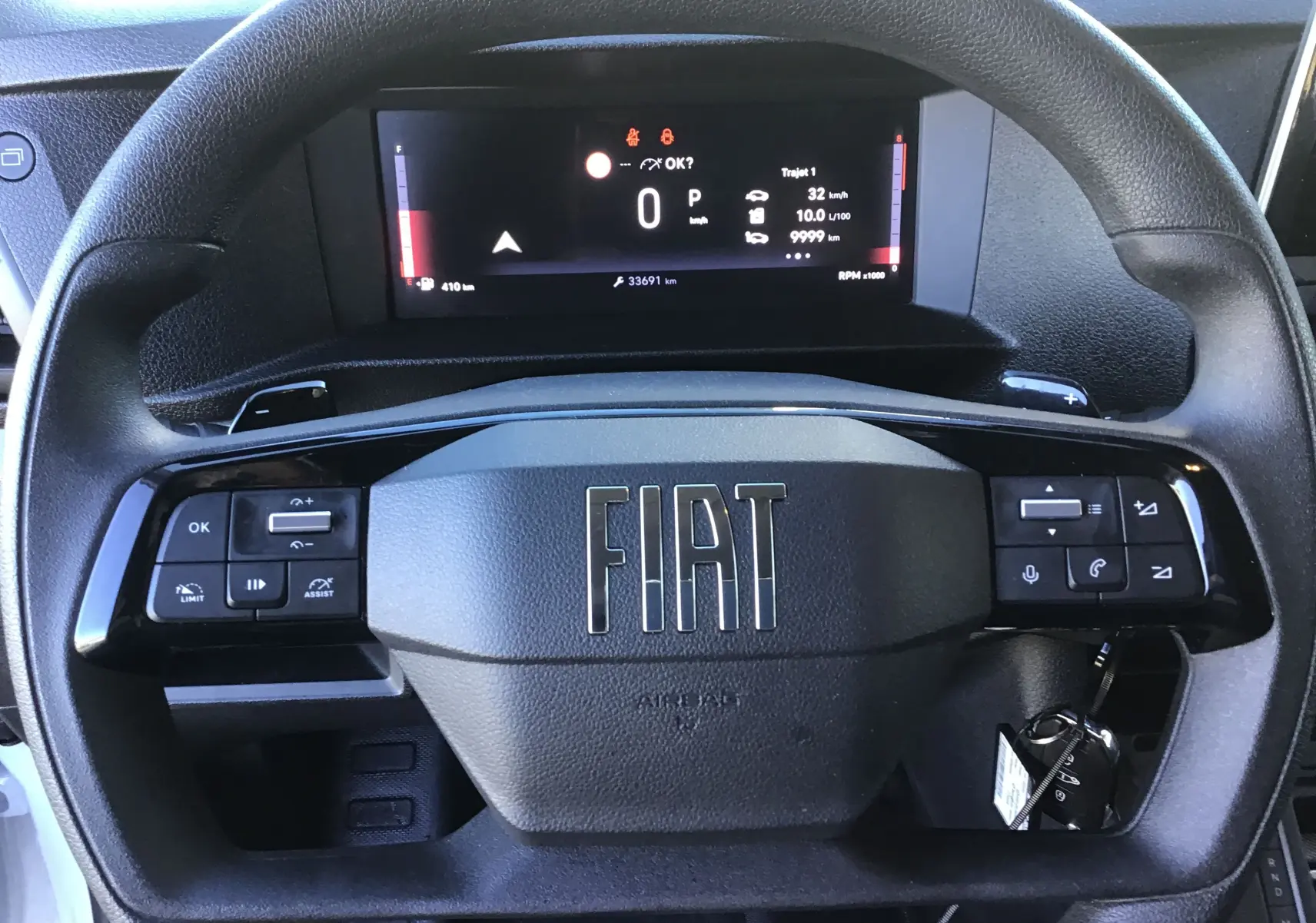 Vue rapprochée du volant noir FIAT avec commandes intégrées et tableau de bord numérique affichant les informations de conduite.