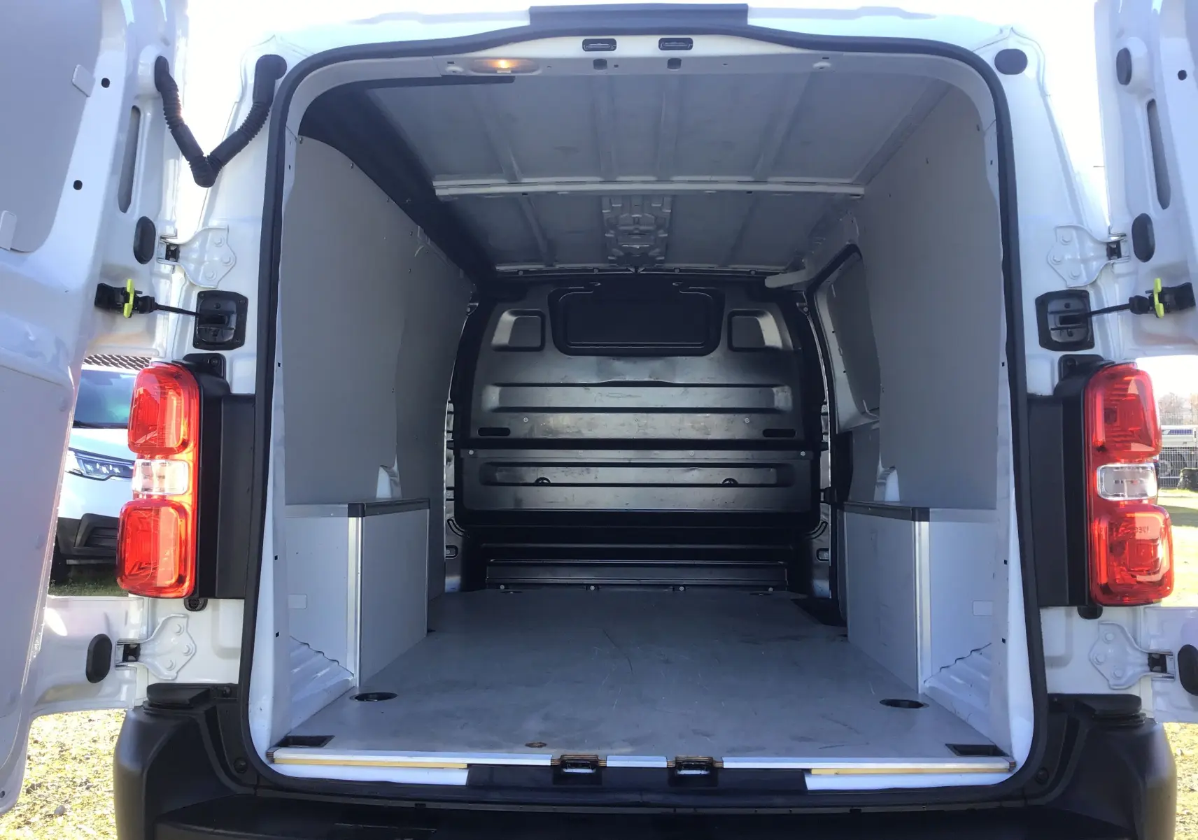 Vue arrière ouverte du fourgon blanc FIAT Scudo XL 2024 montrant l'espace de chargement vide avec protections latérales et plancher bois.