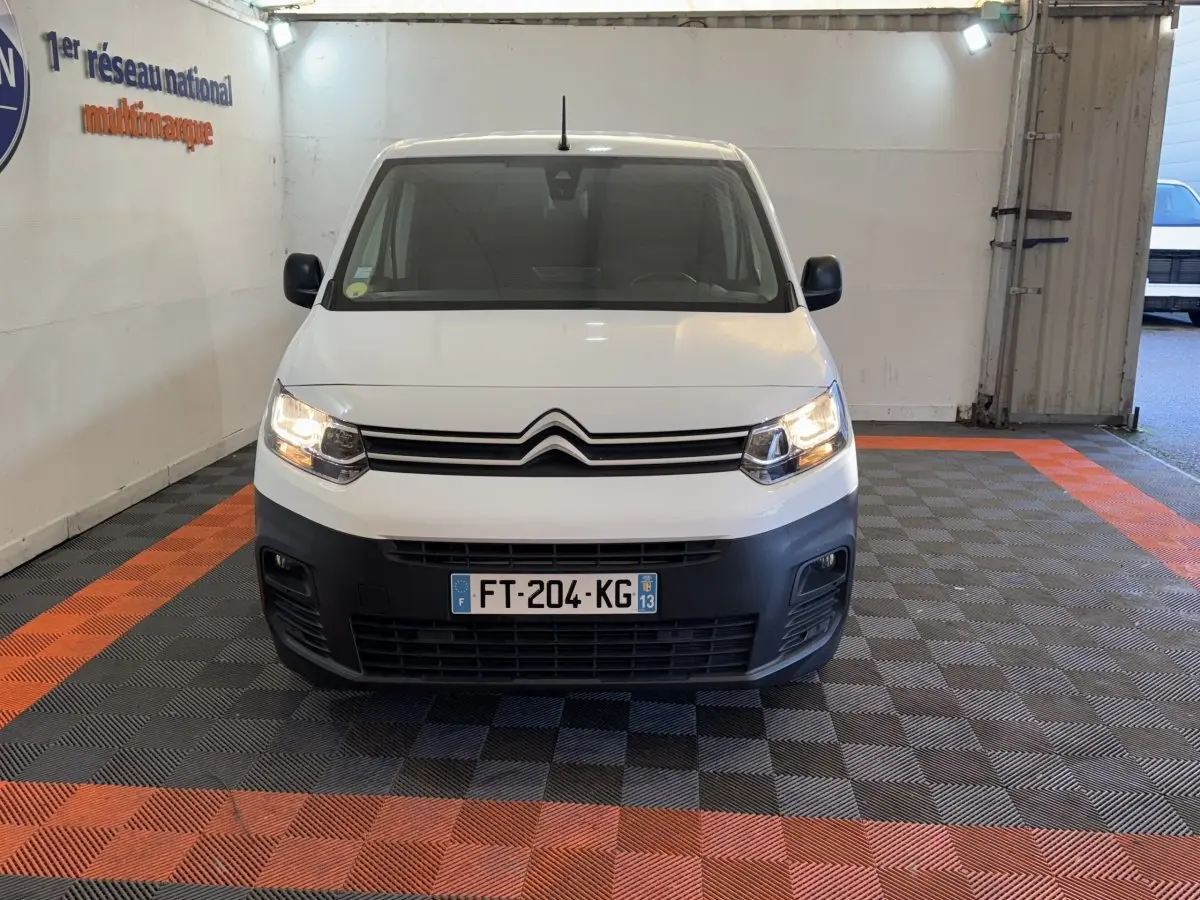 Vue avant d'un Citroën Berlingo blanc 2020 avec calandre noire et phares allumés dans un garage.