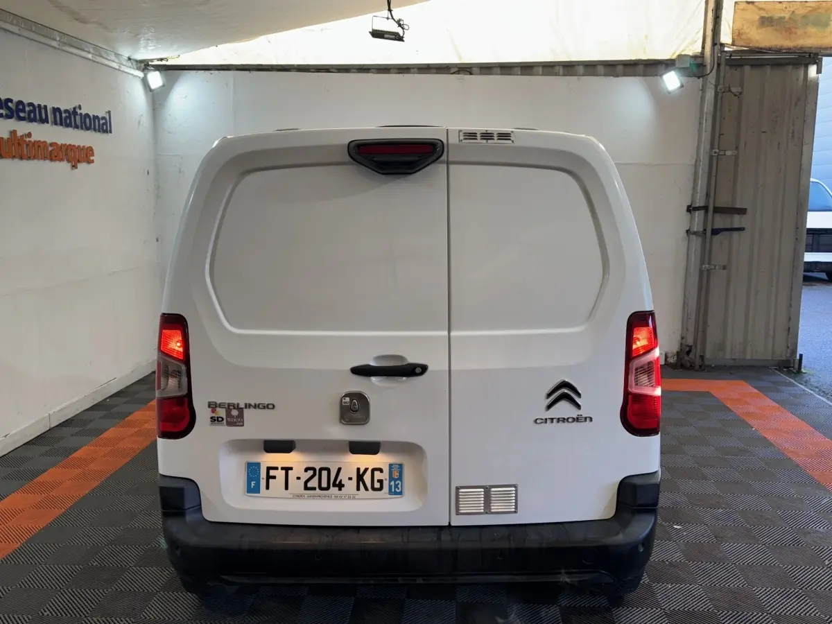 Vue arrière d’un utilitaire Citroën Berlingo blanc avec portes battantes fermées et feux arrière allumés.
