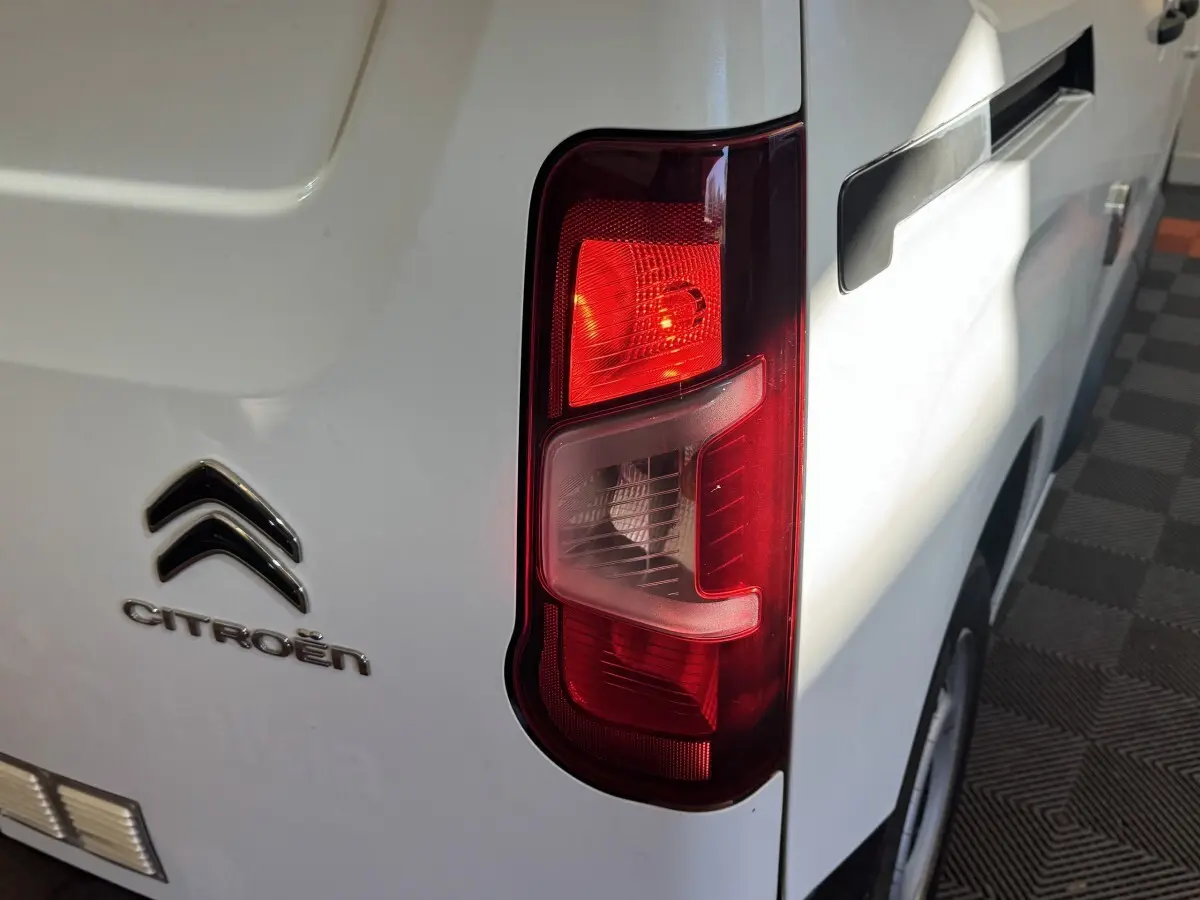 Gros plan sur le feu arrière droit d’un Citroën Berlingo blanc, avec logo et poignée de porte visibles.