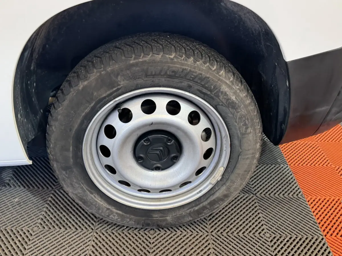 Gros plan sur la roue avant gauche en jante acier du Citroën Berlingo blanc, avec pneu Michelin visible.