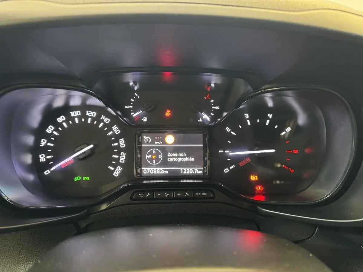 Vue rapprochée du tableau de bord digital du Citroën Berlingo blanc, affichant la navigation et compteurs allumés.