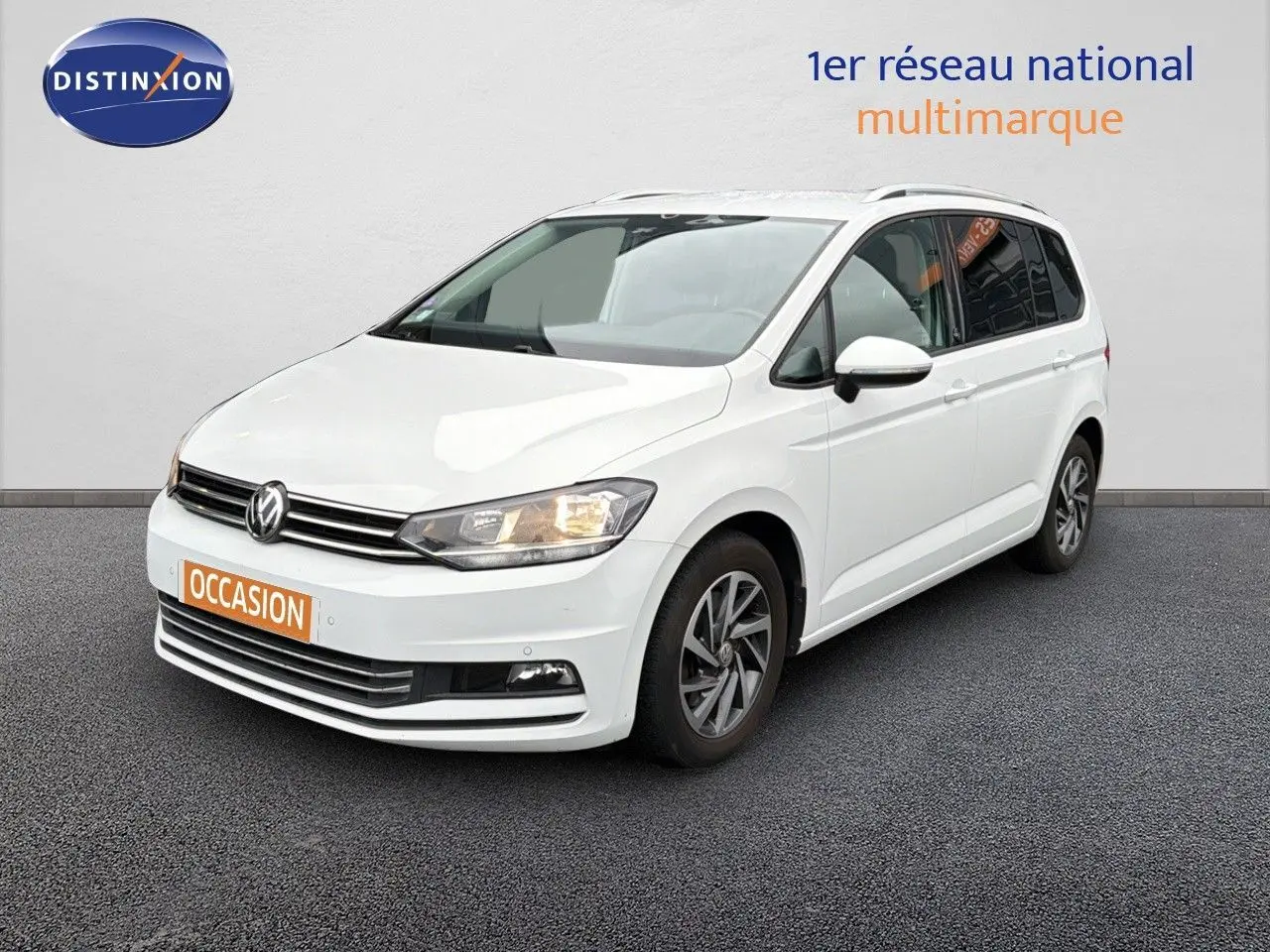 Volkswagen Touran blanc en 3/4 avant droit avec jantes alliage et feux allumés sur fond neutre.