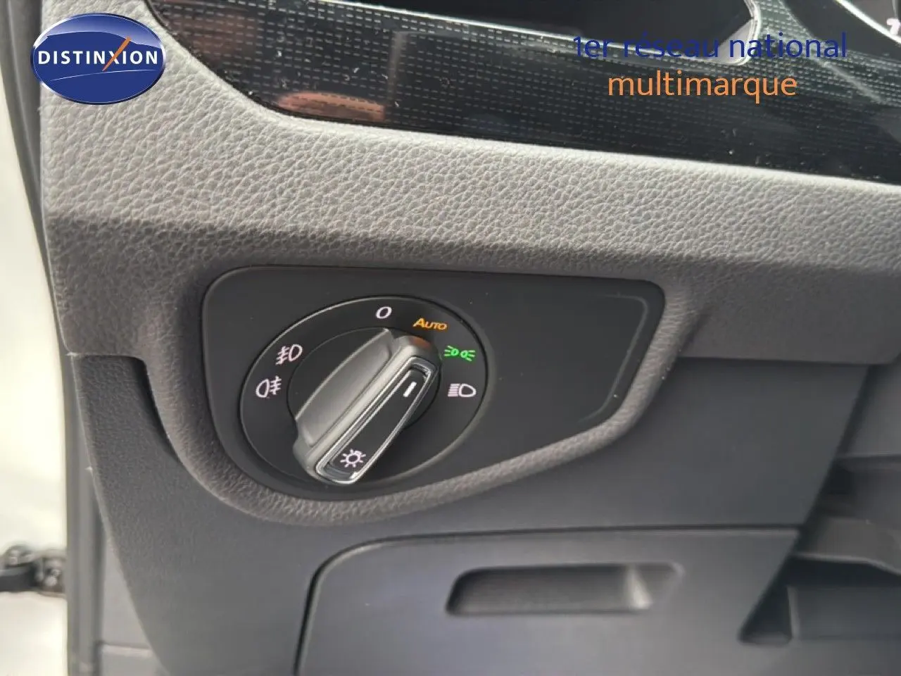 Détail du bouton de commande des phares sur le tableau de bord du Volkswagen Touran blanc, vue intérieure côté conducteur.