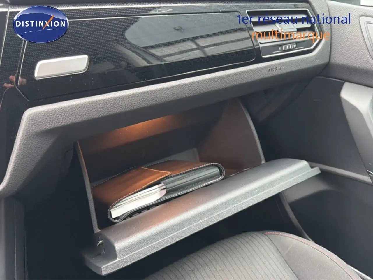 Vue intérieure du coffre à gants ouvert côté passager du Volkswagen Touran blanc, avec un carnet à l'intérieur.