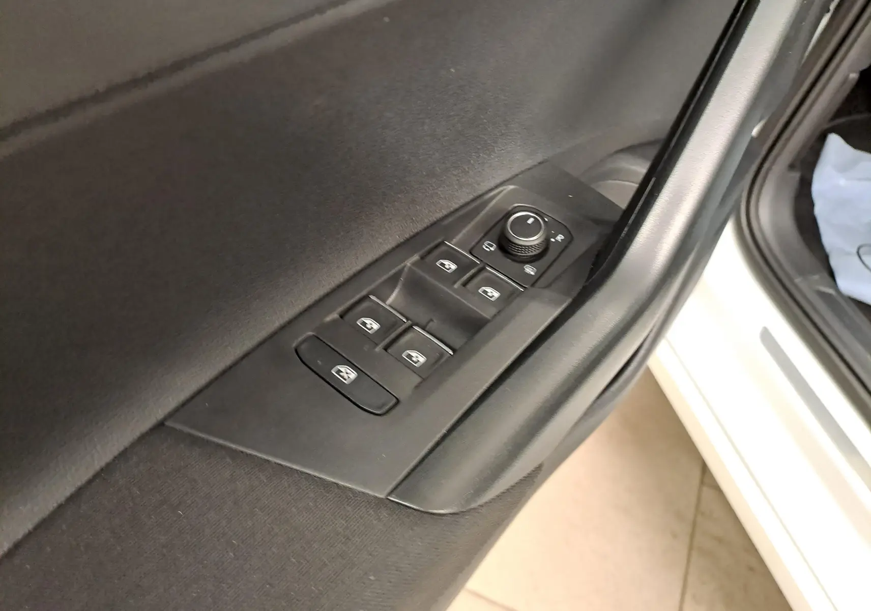 Gros plan sur la commande des vitres et rétroviseurs côté gauche d’un Volkswagen Taigo blanc toit noir, porte ouverte.