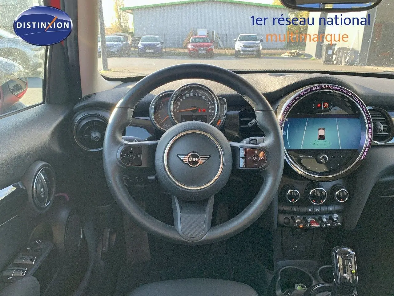 Vue intérieure centrée sur le volant et le tableau de bord d'une MINI rouge chili de 2023 avec écran central digital.