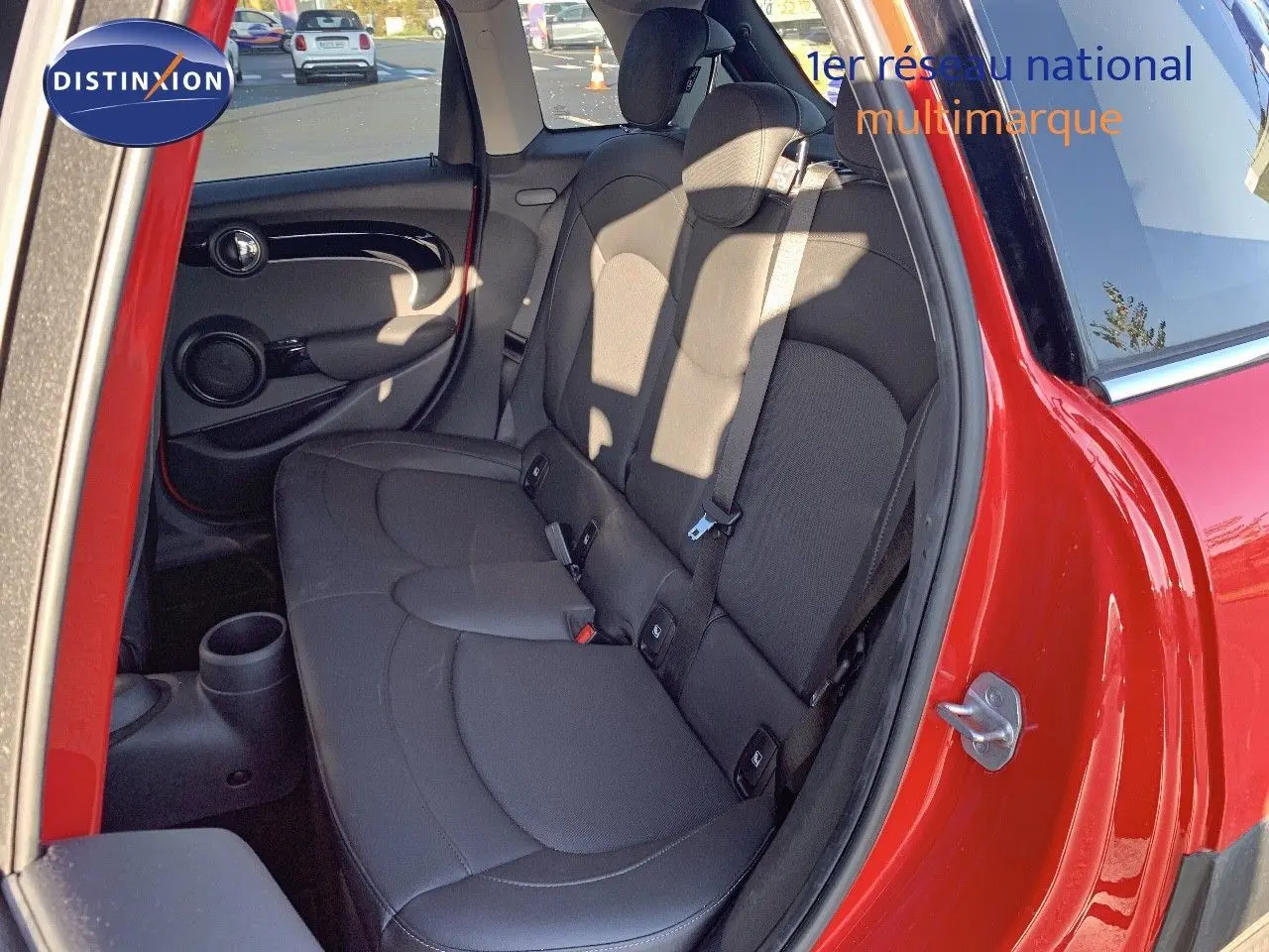 Vue côté gauche arrière sur l'intérieur d'une MINI rouge chili, mettant en valeur les sièges arrière noirs et la porte ouverte.