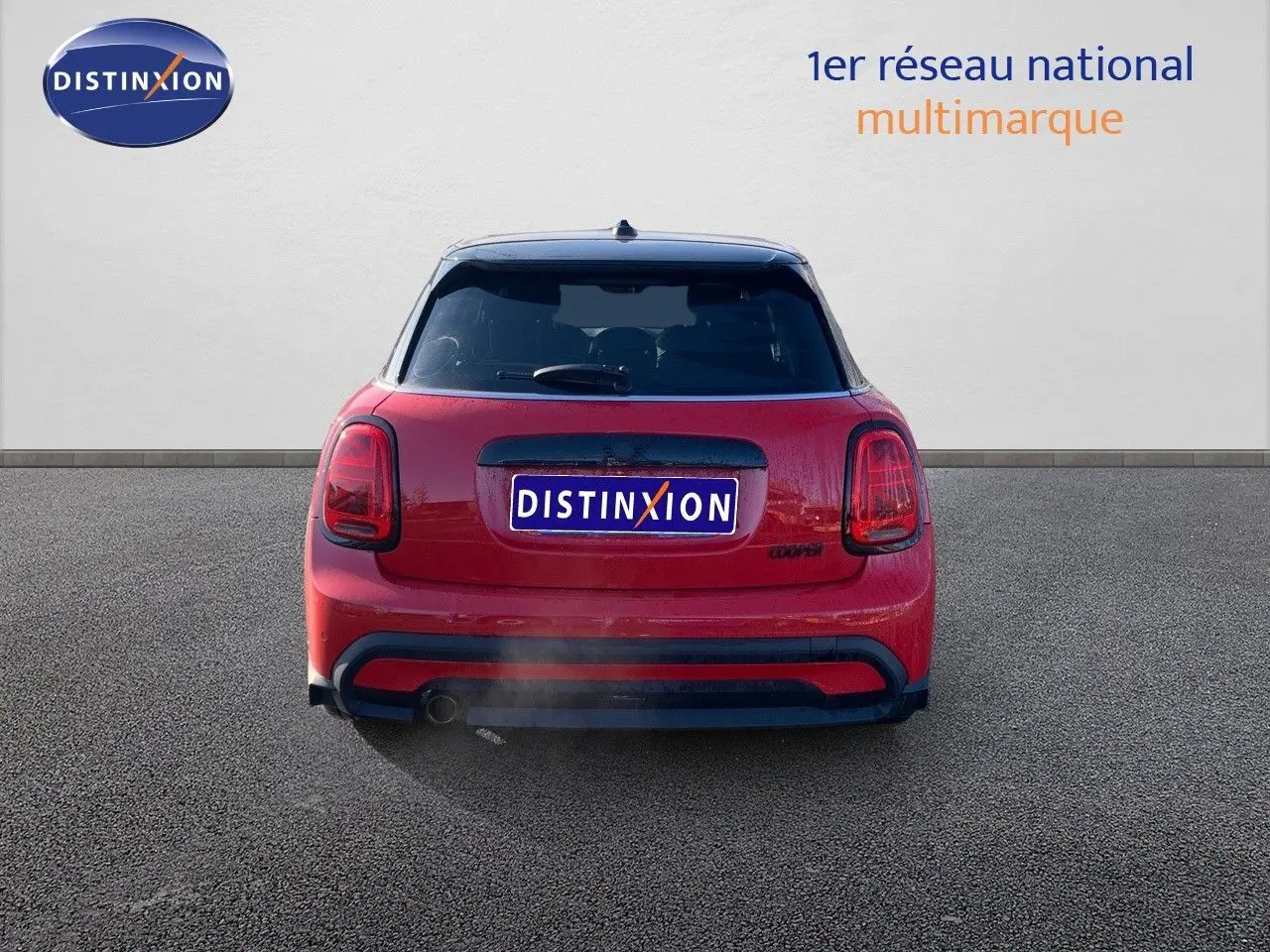 Vue arrière d'une MINI rouge chili 2023 avec toit noir et feux arrière caractéristiques allumés.