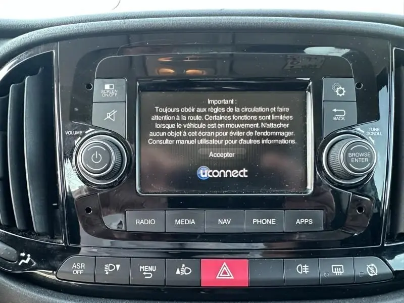 Écran central tactile du tableau de bord du Fiat Doblo Cargo gris foncé, avec commandes multimédia et avertissements affichés.