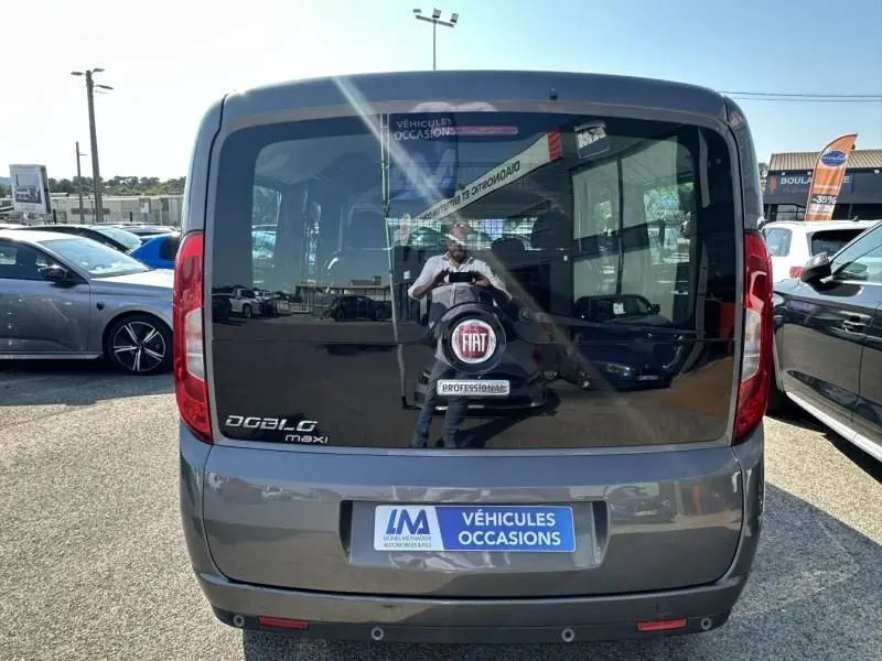 Vue arrière d'un FIAT Doblo Cargo Maxi gris foncé 2021 avec vitres teintées et logo FIAT visible sur la porte arrière.