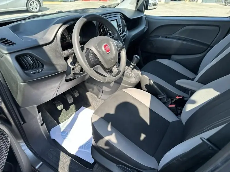 Vue intérieure côté conducteur du Fiat Doblo Cargo 2021, volant avec logo rouge et sièges bicolores gris et noir.
