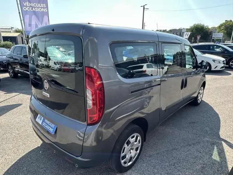 Vue 3/4 arrière droite d'un FIAT Doblo Cargo gris foncé avec vitres latérales teintées sur un parking.