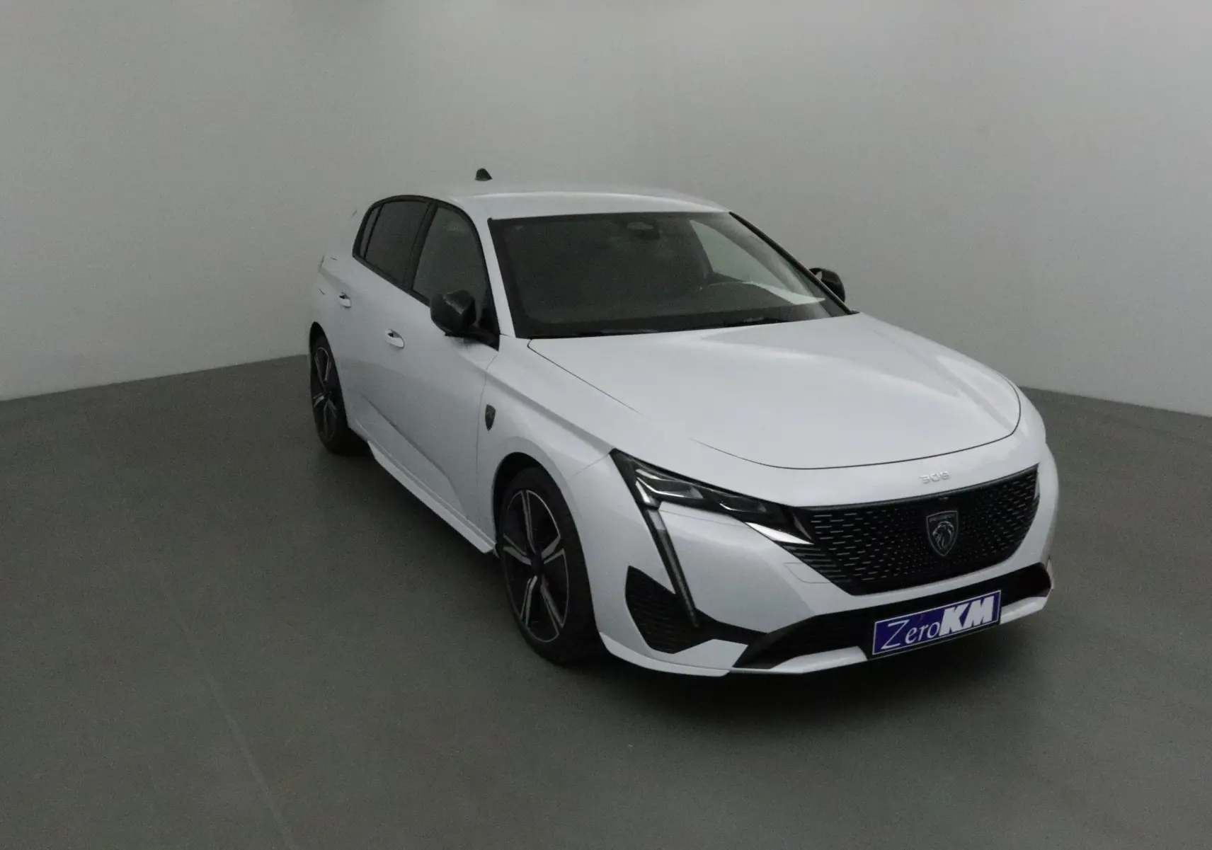 PEUGEOT 308 blanc Okenite en vue 3/4 avant droit, avec calandre noire et jantes alliage distinctives.