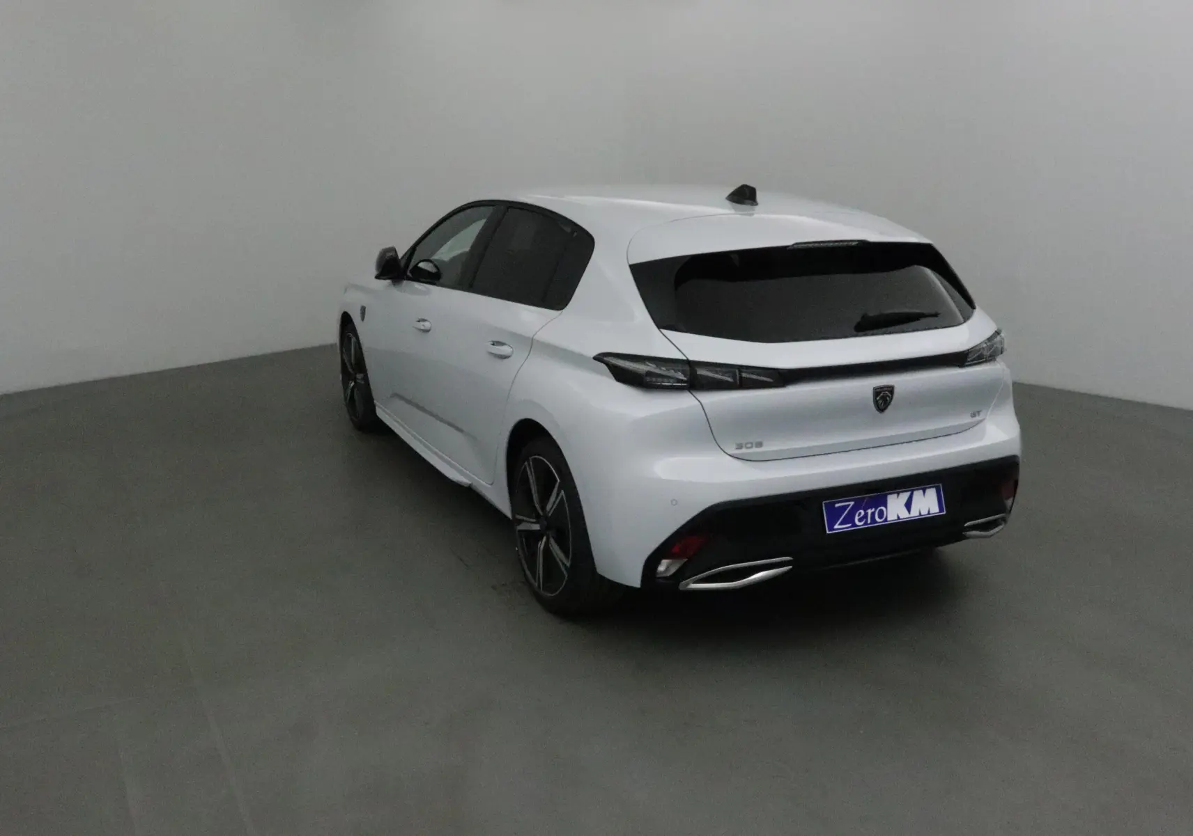 Vue 3/4 arrière droite d'une Peugeot 308 blanche Okenite, avec jantes alliage et vitres teintées dans un studio gris.
