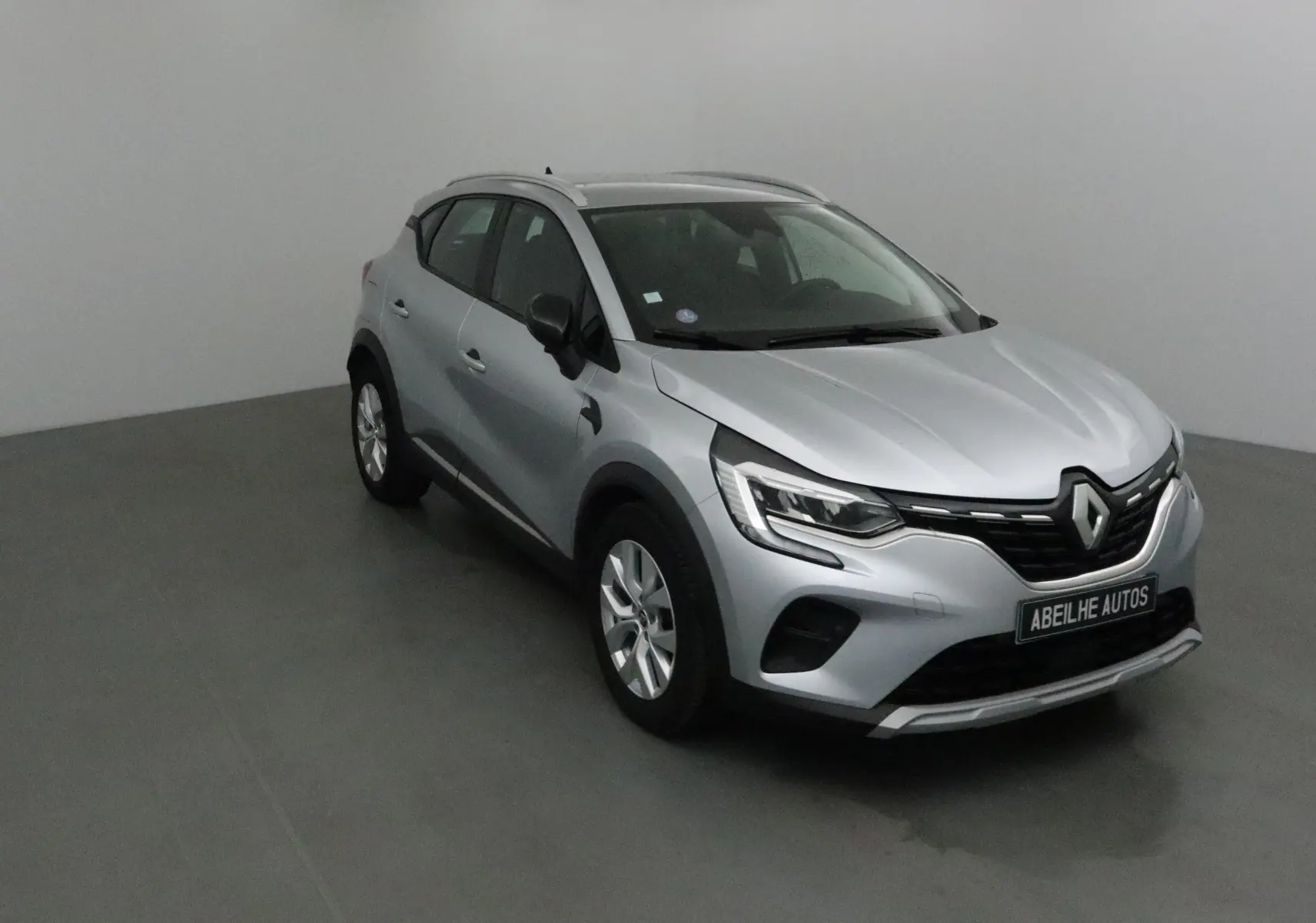 Renault Captur gris Highland en 3/4 avant droit, mettant en valeur ses optiques LED et sa calandre noire distinctive.