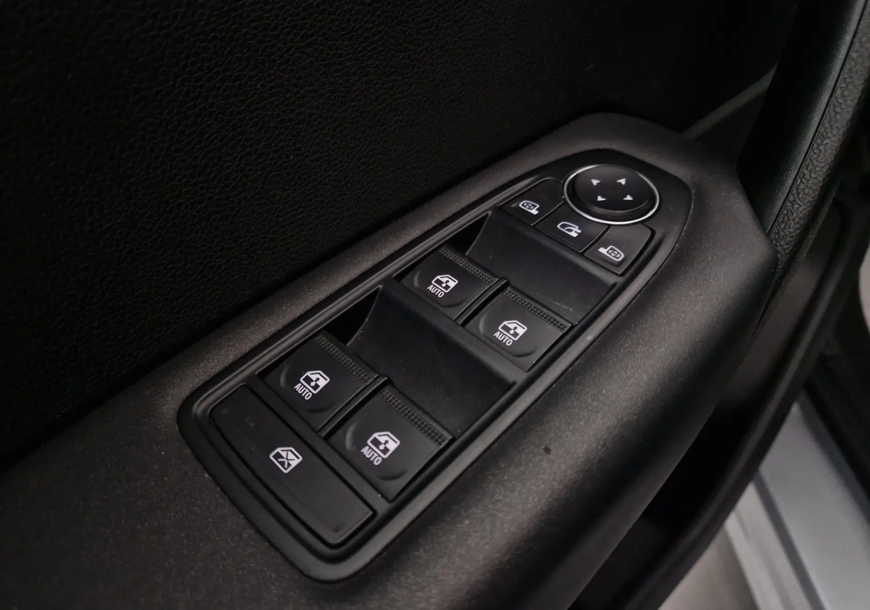 Gros plan sur les commandes des vitres électriques et rétroviseurs côté conducteur d’un Renault Captur gris Highland.