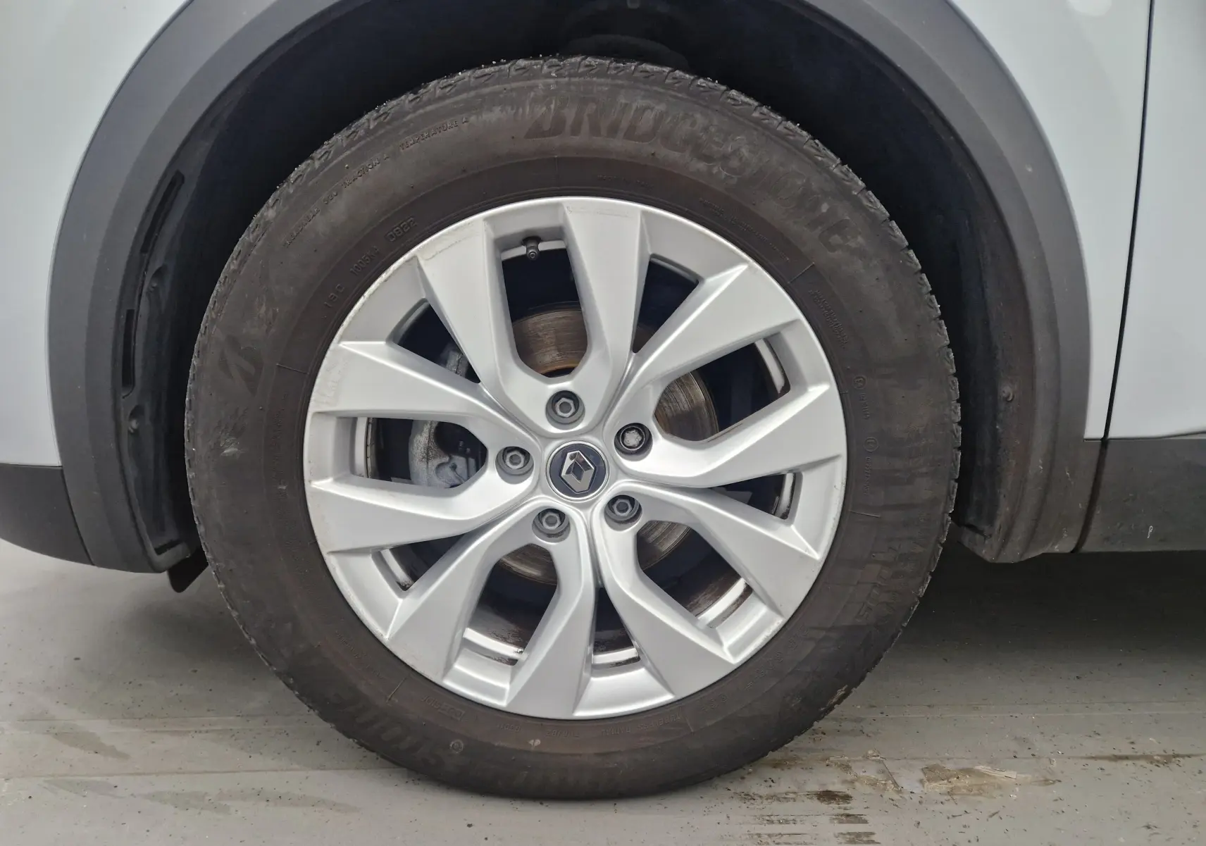 Gros plan sur la roue avant droite d’un Renault Captur gris Highland avec jante alliage 17 pouces et logo Renault central.