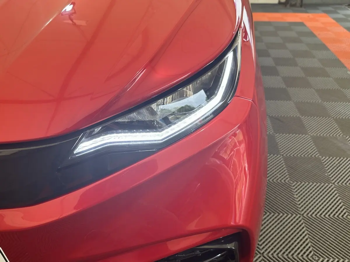 Gros plan sur le phare avant gauche d'une Aixam Ambition 0.5 City Sport rouge avec éclairage LED distinctif.