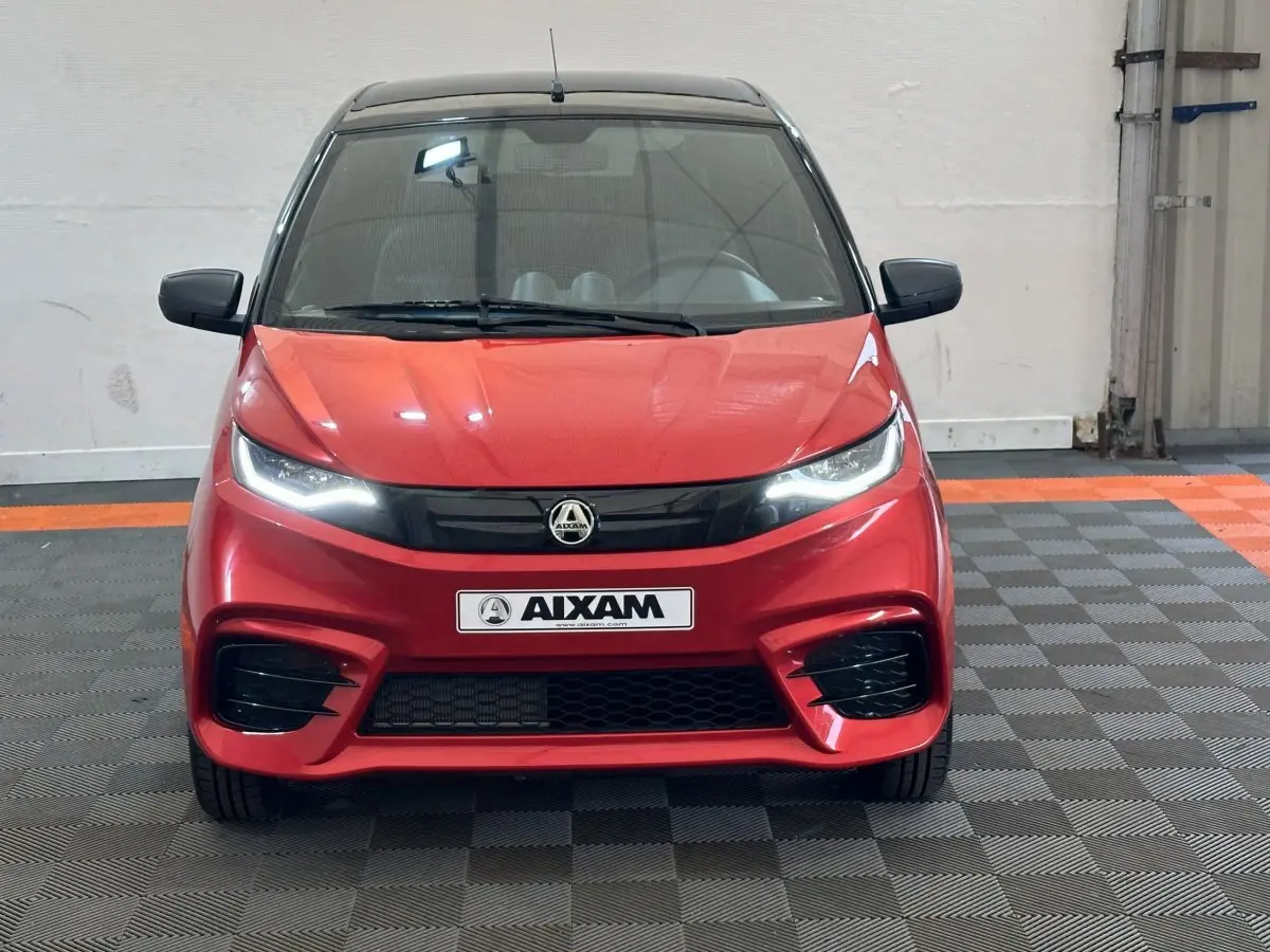 Vue de face d'une Aixam Ambition 0.5 City Sport rouge avec phares allumés et calandre noire brillante.