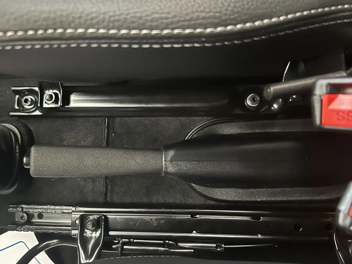 Vue rapprochée de la poignée de frein à main noire et du mécanisme sous le siège d’une Aixam Ambition 0.5 City Sport.