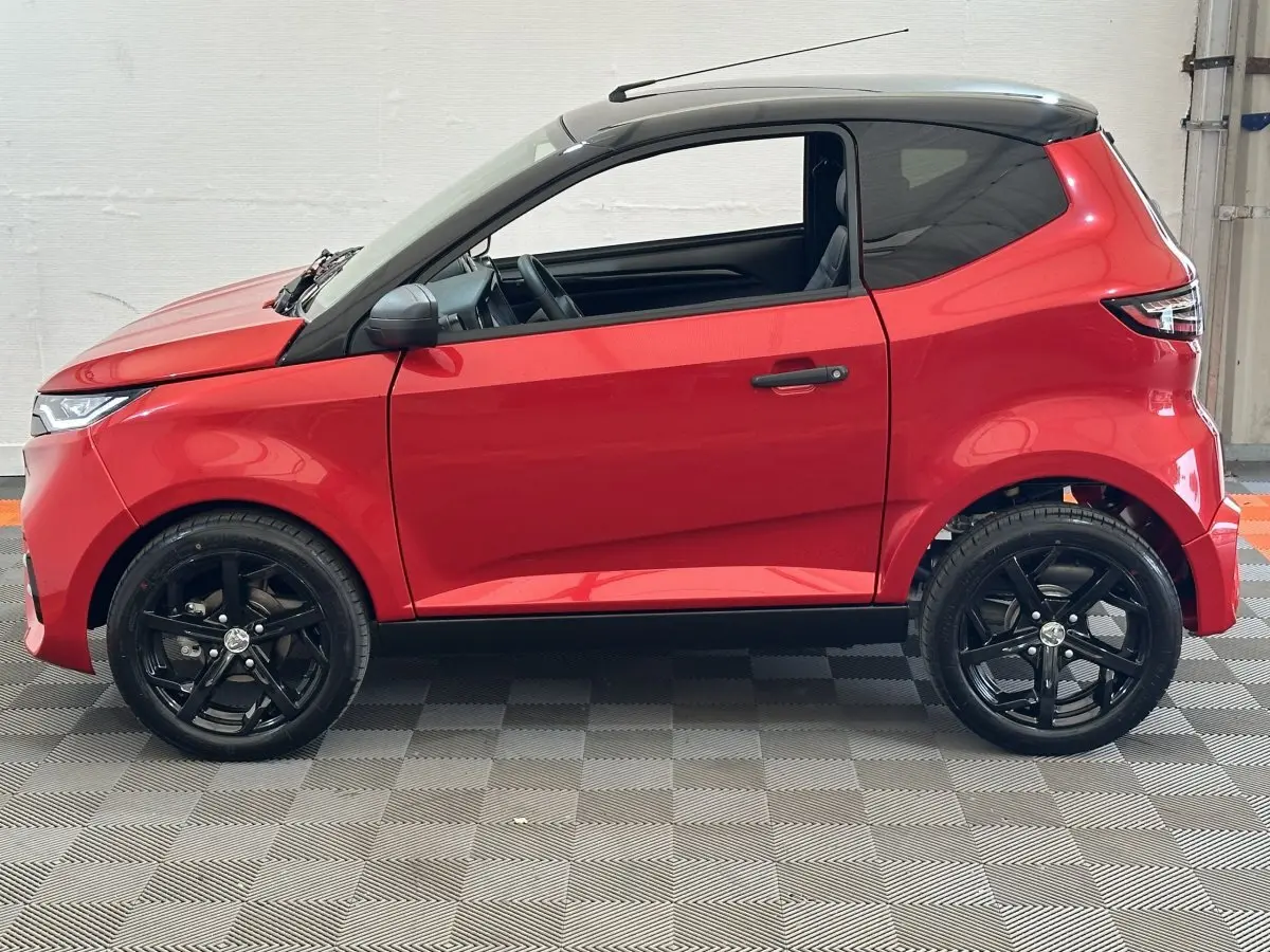 Vue de profil côté gauche d'une Aixam Ambition 0.5 City Sport rouge avec toit noir et jantes noires.