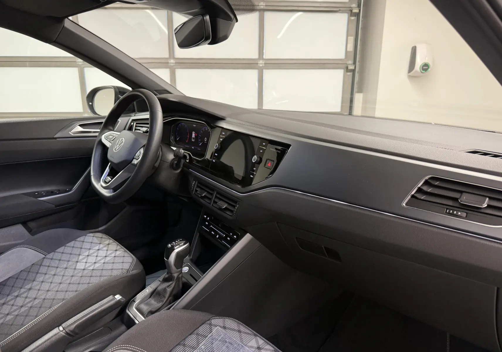 Vue intérieure côté conducteur du Volkswagen Taigo 2025, tableau de bord noir et sièges tissu à motif géométrique.