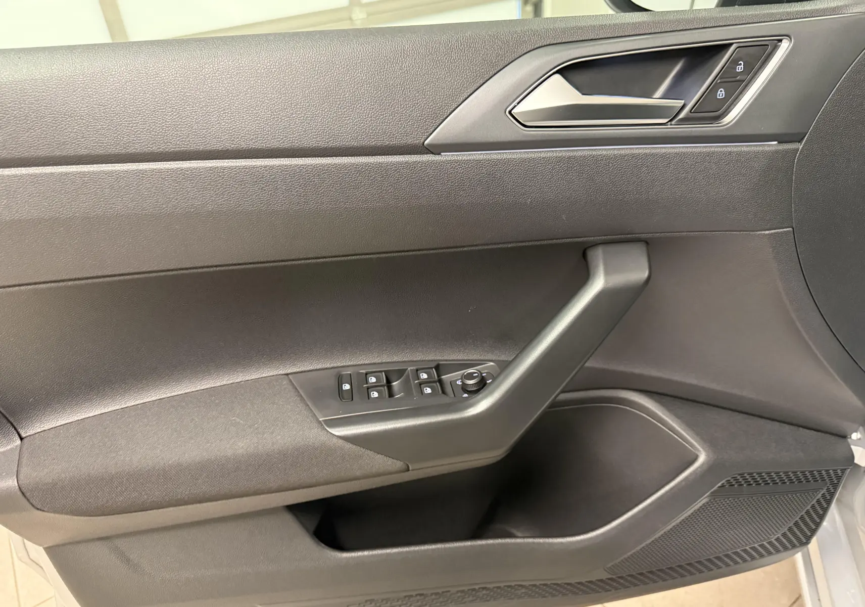 Gros plan sur la porte intérieure côté conducteur du Volkswagen Taigo 2025, avec commandes de vitres et verrouillage en plastique noir.