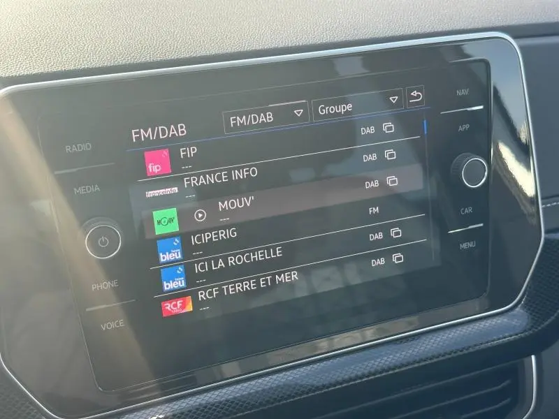 Écran tactile multimédia du Volkswagen T-Cross 1.0 TSI R-Line 2026 affichant les stations FM/DAB, intérieur noir.