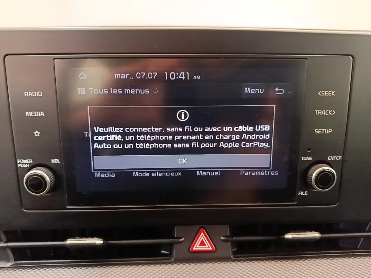 Écran tactile central du tableau de bord du Kia Sportage beige, avec commandes physiques autour et affichage de connexion Apple CarPlay.