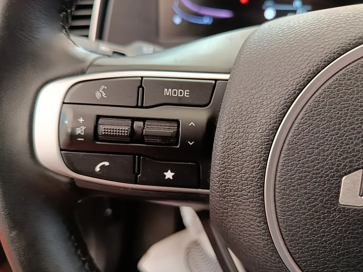 Gros plan sur les commandes du volant cuir noir du Kia Sportage beige, boutons multifonctions visibles.