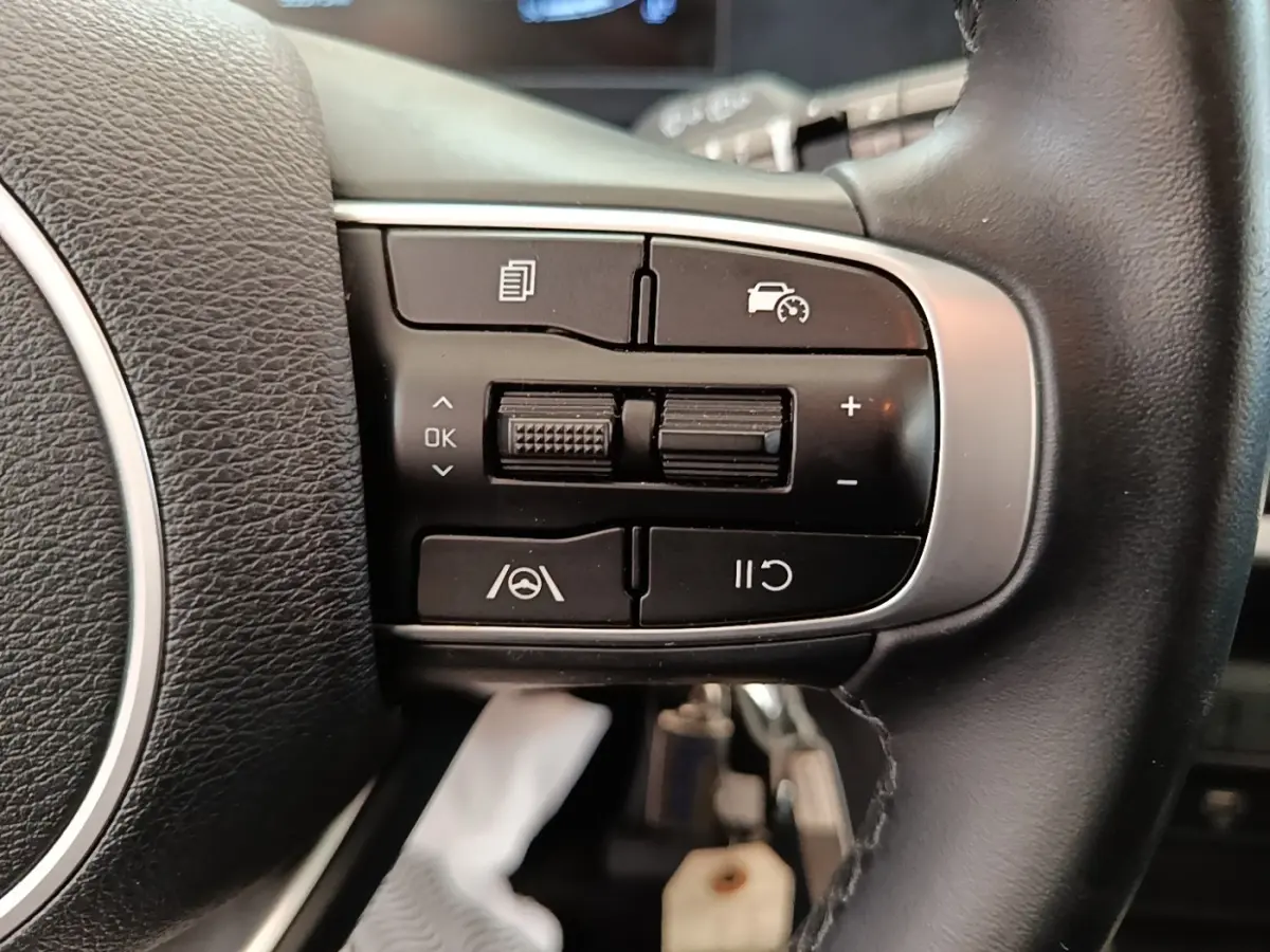 Gros plan sur les commandes multifonctions noires du volant cuir du KIA SPORTAGE beige 2022, côté gauche.