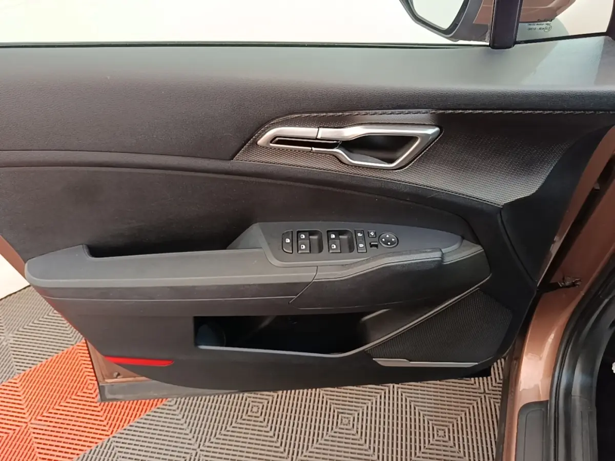 Intérieur côté gauche de la porte avant beige du KIA SPORTAGE 2022 avec commandes électriques et poignée argentée.