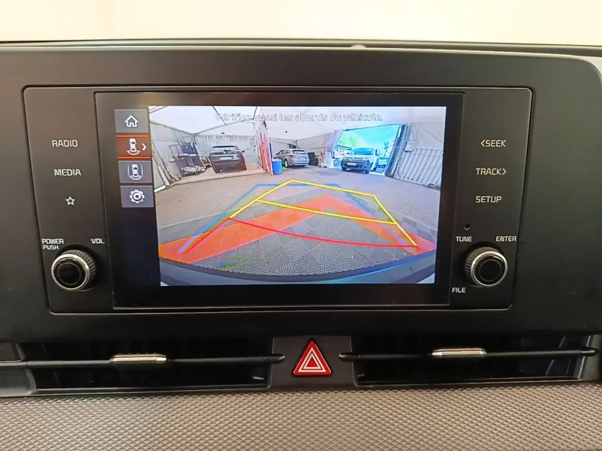 Écran tactile affichant la caméra de recul avec lignes de guidage colorées dans un Kia Sportage beige.