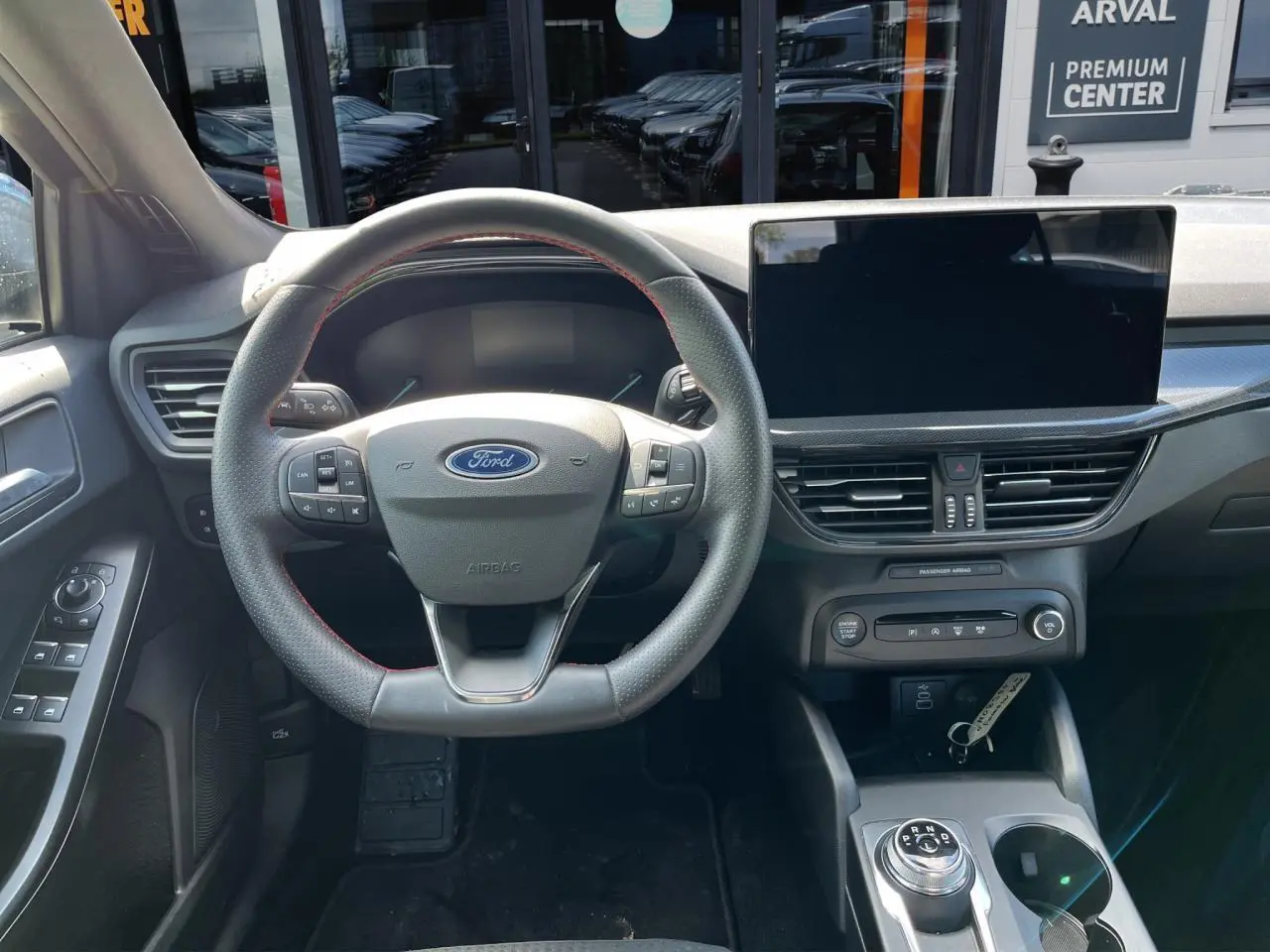 Vue intérieure du poste de conduite de la Ford Focus SW 2025, volant avec surpiqûres rouges et écran tactile central.