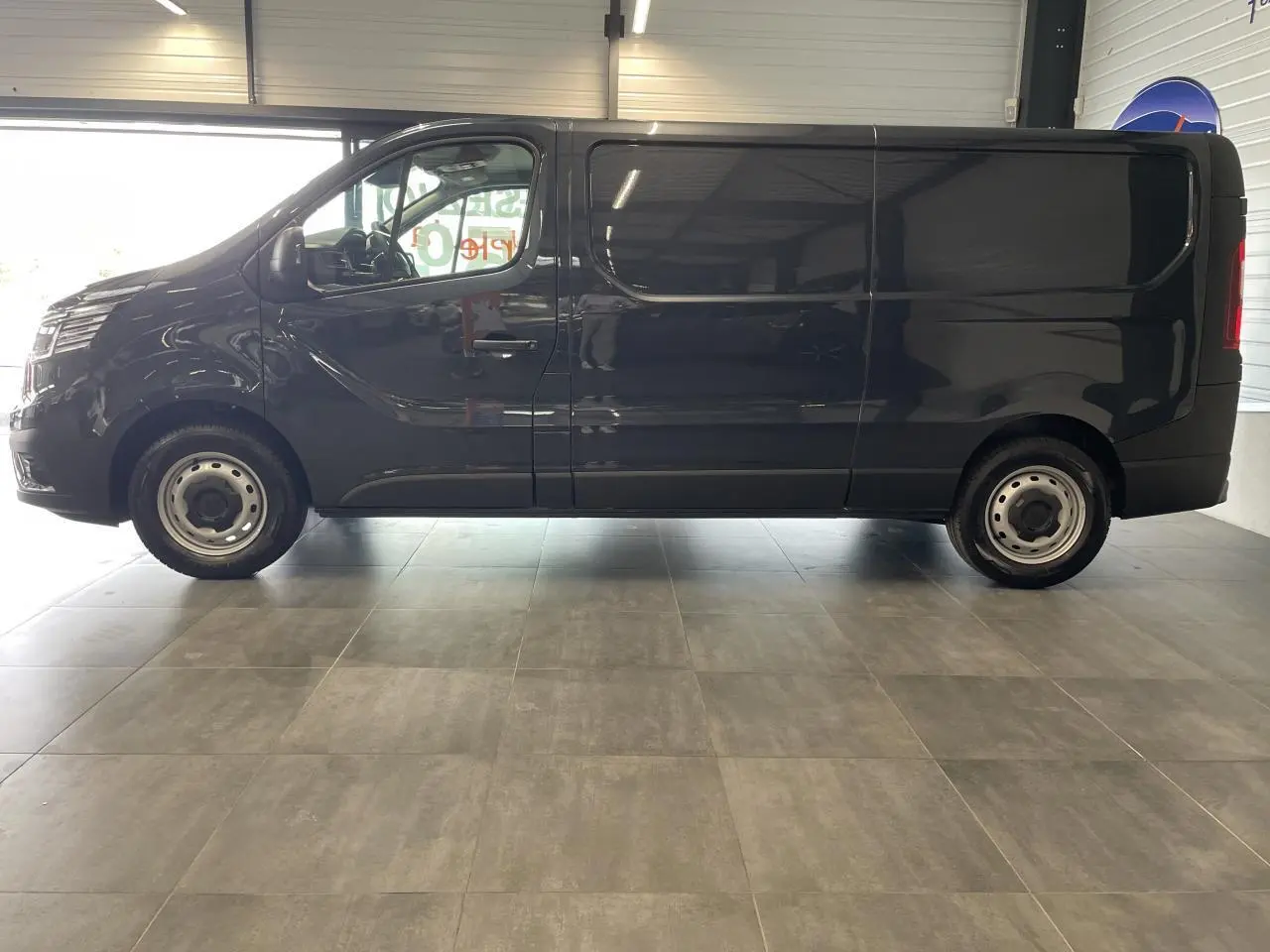 Profil latéral droit d'un Renault Trafic Fourgon gris foncé avec jantes tôles et vitres teintées en showroom.