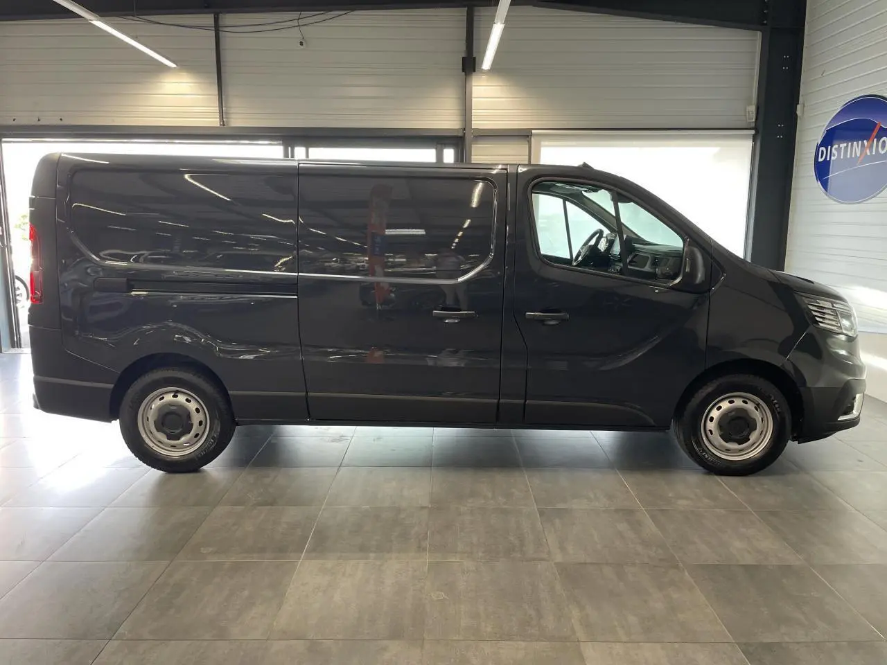 Profil droit du Renault Trafic Fourgon L2H1 2025 en gris comète, avec jantes tôles et porte coulissante fermée.